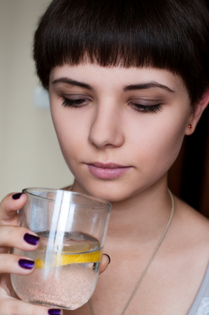 beautiful girl with a short hairstyle looking at the cold water with ice and lemonの写真素材