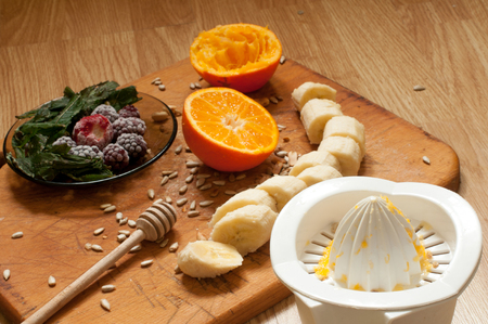 cooking,hand squeezes orange juice, banana,frozen strawberries blackberries and seeds vivid smoothie ingredients and blender, juicer, tulips on the background on woodenの写真素材