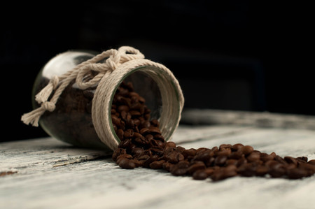 scattered coffee beans in a jar on woodenの写真素材