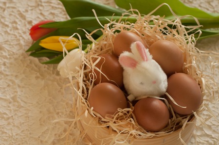 Easter holiday basket with eggs, flowers and easter bunny on rustic wooden Easter rabbit with eggs tulipsの写真素材