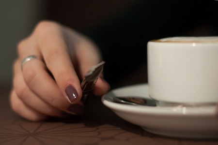 Close-up female hands holding cup with coffee cappuccino with foam Perfect red gel polish manicure.の写真素材