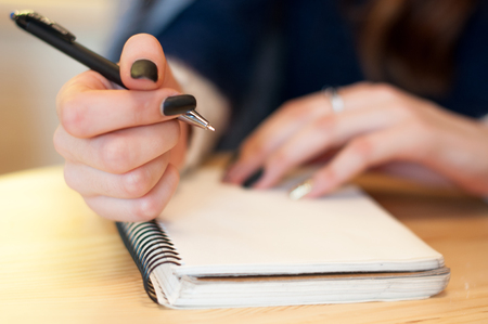 paper in business woman beautiful female hand writing notes on a table black manicure and blank letterの写真素材