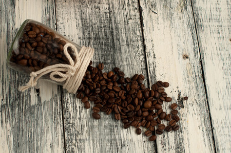 scattered coffee beans in a jar on woodenの写真素材