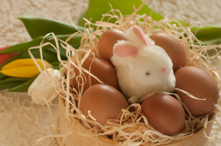 Easter holiday basket with eggs, flowers and easter bunny on rustic wooden Easter rabbit with eggs tulipsの写真素材