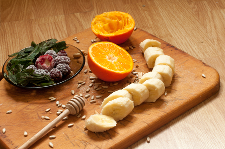 cooking,hand squeezes orange juice, banana,frozen strawberries blackberries and seeds vivid smoothie ingredients and blender, juicer, tulips on the background on woodenの写真素材