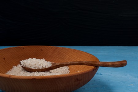 Raw rice in wooden bowl with wooden spoon on blue background.の写真素材