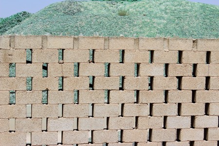 A mountain of small fragments of green glass from broken bottles for recycling behind a brick wallの写真素材