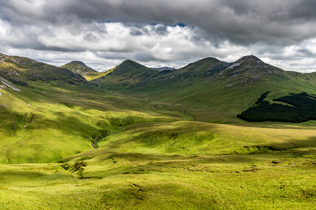 The view of a green valley in Ireland's Connemara National Park with the Twelve Bens Mountains in...