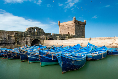 A fleet of blue fishing boats huddled together in the port of Essaouira in Morocco. You can also see the fortifications and a tower of the citadel of Mogadorの写真素材