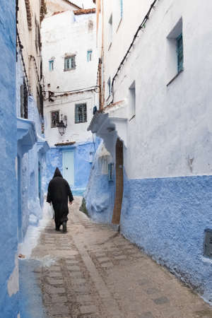 In the medina of Chefchaouen in Morocco. A man dressed in the traditional Berber coat walks down an alley lined with blue wallsのeditorial素材
