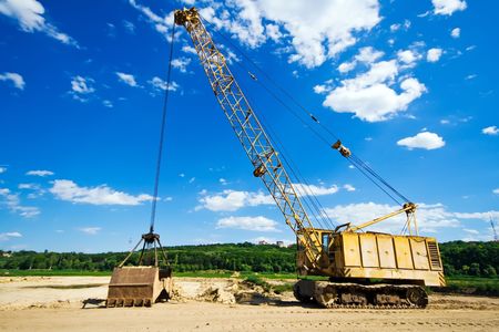Old yellow excavator moving sand under blue skyの写真素材
