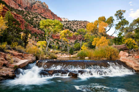 A cascade with fall color and red cliffs in Zion Canyon, Zion National Park, Utahの写真素材