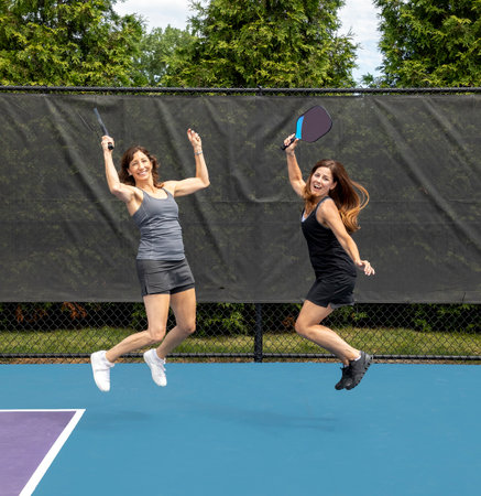 Two pickleball players jumping with paddles on a court during summer.の写真素材