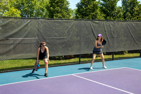 A pickleball player serves while her partner prepares for a return on a suburban pickleball court during summer.の写真素材