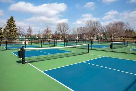 View of a pickleball complex with blue and green courts beside a playground in a suburban park in early spring.の写真素材