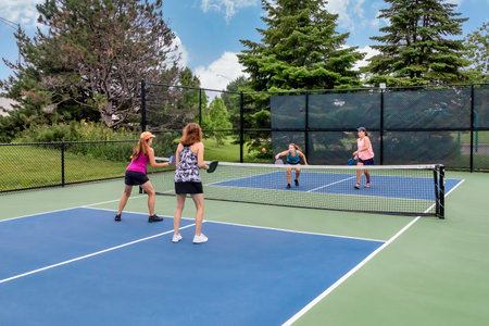 A comptetivie doubles game of pickleball with a group of women on a blue and green court in summer.の写真素材