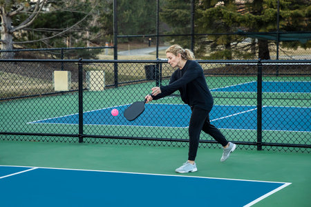 A female pickleball player prepares to serve a bright pink ball on a blue and green court in early spring.の写真素材
