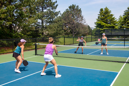 A competitive doubles game of pickleball at the net on a blue and green court in summer.の写真素材