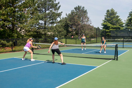 Two players approach the net in a competitive doubles game of pickleball on a blue and green court in summer.の写真素材