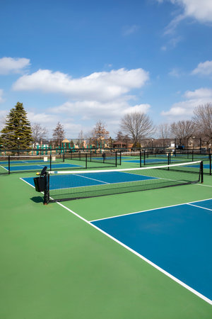 View of a pickleball complex with blue and green courts beside a playground in a suburban park in early spring.の写真素材