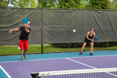 A pickleball player serves while his partner prepares for a return on a suburban pickleball court during summer.の写真素材