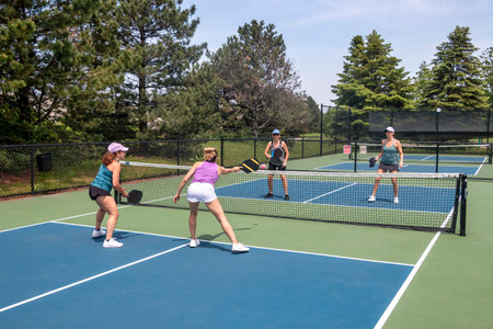 A competitive doubles game of pickleball at the net on a blue and green court in summer.の写真素材