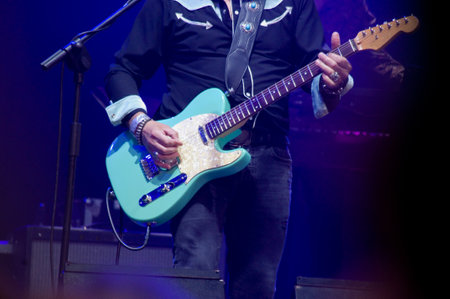 A musician playing an aquamarine green electric guitar on stage during a concert