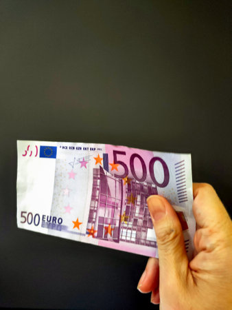 A â‚¬500 note fastened with one hand with dark background with space for copying