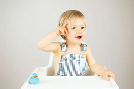 Blond baby with striped overalls sitting in the high chair and smilingの写真素材