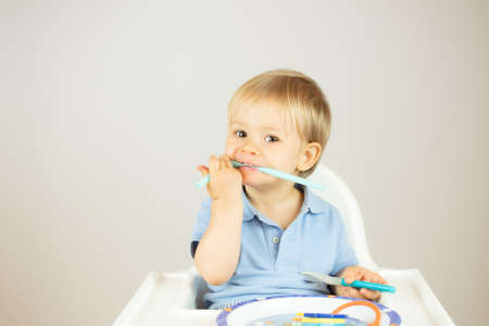 Blond baby with blue polo shirt sitting in the high chair and gesturingの写真素材