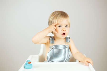 Blond baby with striped overalls sitting in the high chair and smilingの写真素材