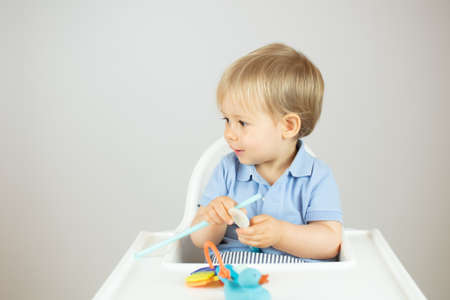 Blond baby with blue polo shirt sitting in the high chair and gesturingの写真素材
