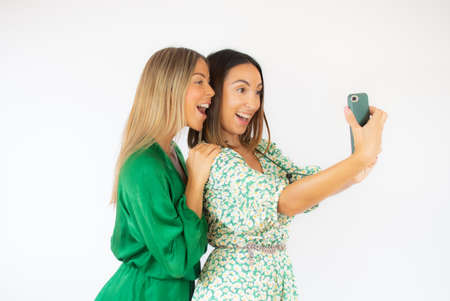 Two friends in green dresses with a mobile smilingの写真素材