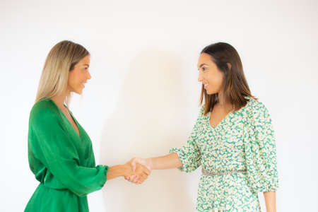 Two smiling women in green dress shake handsの写真素材