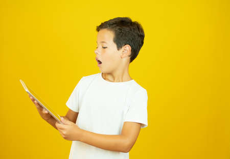 Boy in white shirt looking surprised at his tabletの写真素材
