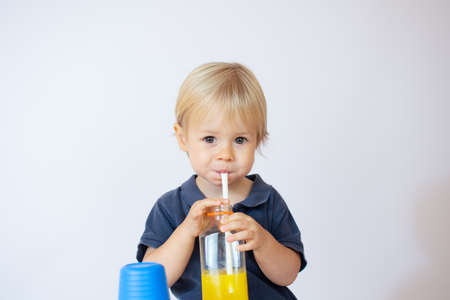 Beautiful blond baby sitting drinking juice through a strawの写真素材