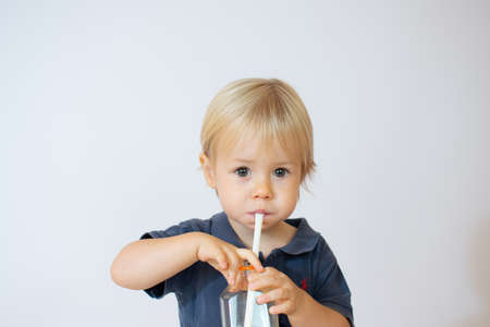 Beautiful blond baby sitting drinking juice through a straw