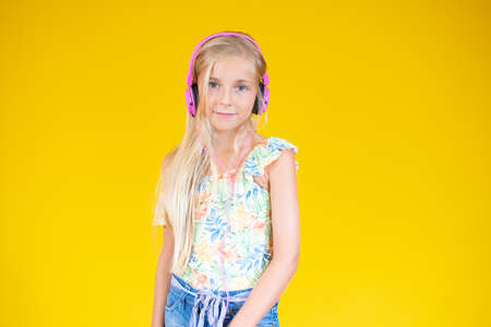 Smiling beautiful blonde girl with headphones on yellow background