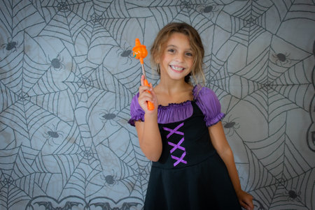 funny child girl in witch costume for Halloween over cobweb backgroundの写真素材