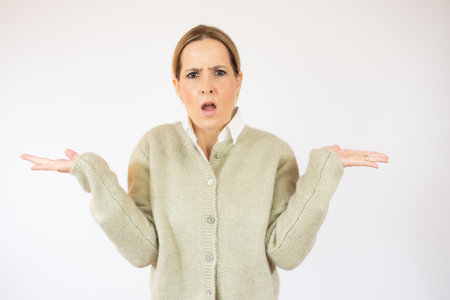 Young woman standing over white isolated background clueless and confused expression with arms and hands raised. Doubt concept.の写真素材