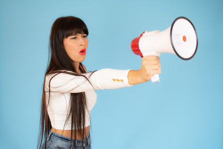 young woman shouting with a megaphone against a blue backgroundの写真素材