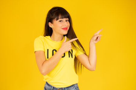 Smiling woman pointing finger side. Isolated portrait on yellow.の写真素材