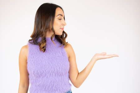 Portrait of a smiling young woman with brunette hair standing over white background, holding fingers crossed for good luckの写真素材
