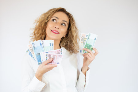 Portrait of a cheerful woman holding money banknotes isolated over white backgroundの写真素材