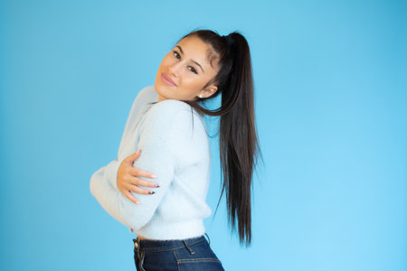 Portrait of a pretty young woman hugging herself standing isolated over blue backgroundの写真素材