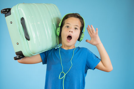 Kid with headphones with his suitcase surprise and shocked facial expression on blue backgroundの写真素材