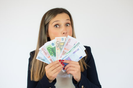 Close up portrait of a exciting young business woman holding money banknotes and celebrating isolated over white backgroundの写真素材