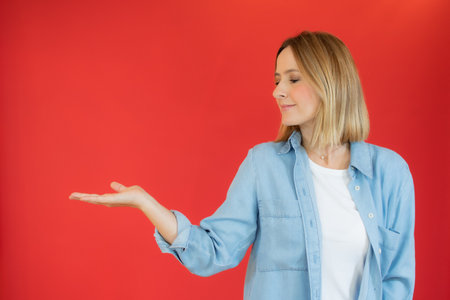 Happy Young Woman in denim shirt Presenting On red Backgroundの写真素材