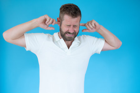 Young man covering his hears over blue background.