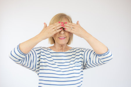 Middle age beautiful woman wearing casual denim shirt standing over pink background covering eyes with hands smiling cheerful and funny. Blind concept.の写真素材